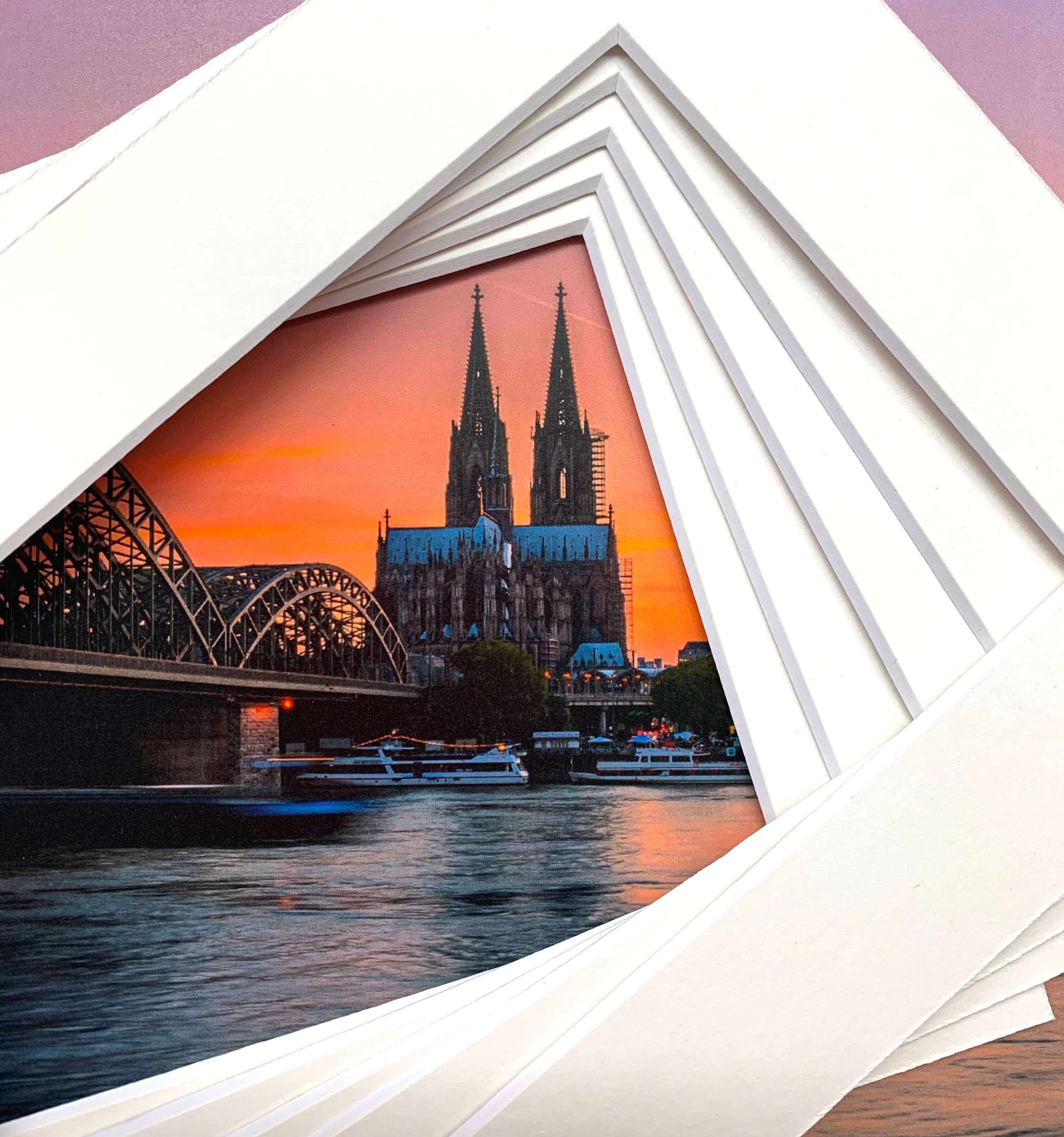 Ein Stapel weiße Passepartouts umranden den Kölner Dom beim Sonnenuntergang